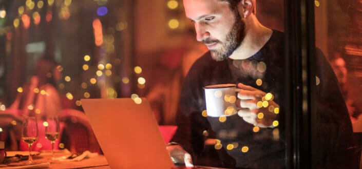 man having coffee while looking at his laptop