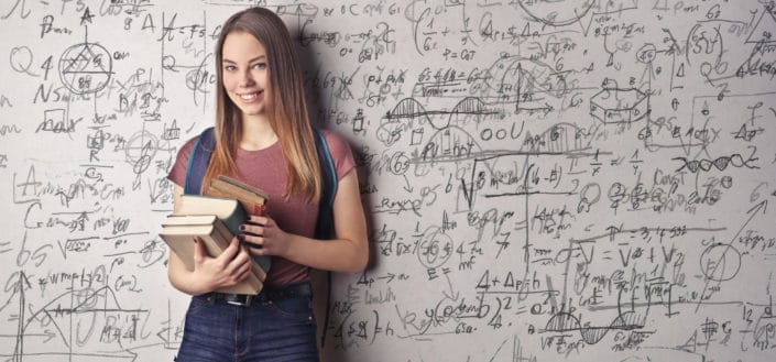woman smiling while holding books with a lot of math formulas at the background