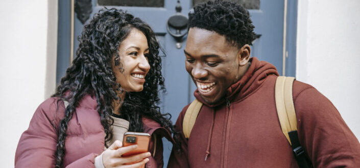 Cheerful couple sharing smartphone on city street