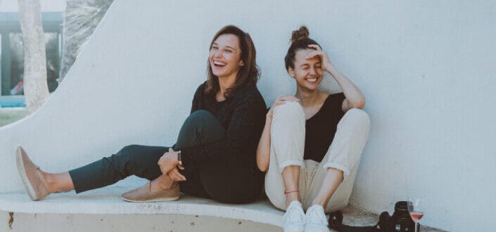 Two girls laughing together while sitting on a white-painted bench.