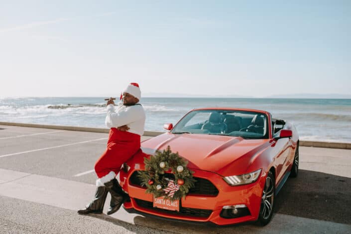Man in Santa Suit Leaning Against A Red Car